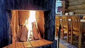 Un feu de bois crépite dans une cabane rustique, agrémentée de meubles en bois et d’un mur en pierre.