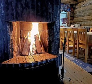 A log fire in a rustic cabin with wooden furniture and a stone wall. - Rukanjurmu 8 | Spacious 2BR Log Apt with Sauna (Ruka)
