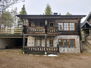 A two-story log cabin with a balcony, a garage, and a stone-patterned exterior. - Rukanjurmu 8 | Spacious 2BR Log Apt with Sauna (Ruka)
