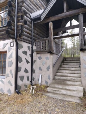 A log cabin with a stone-patterned exterior, a set of concrete stairs, and a metal railing. - Rukanjurmu 8 | Spacious 2BR Log Apt with Sauna (Ruka)