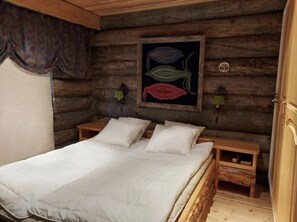 A wooden cabin-style bedroom with a bed, two bedside tables, and a wall-mounted artwork. - Rukanjurmu 8 | Spacious 2BR Log Apt with Sauna (Ruka)