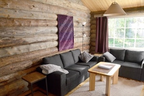 Ein rustikaler Holzblockhaus-Innenraum mit einer Sofagarnitur, einem kleinen Tisch und einer Lampe.