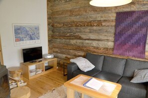 Ein gemütliches Wohnzimmer mit Steinwand, Flachbildfernseher, grauem Sofa und kleinem Holztisch.