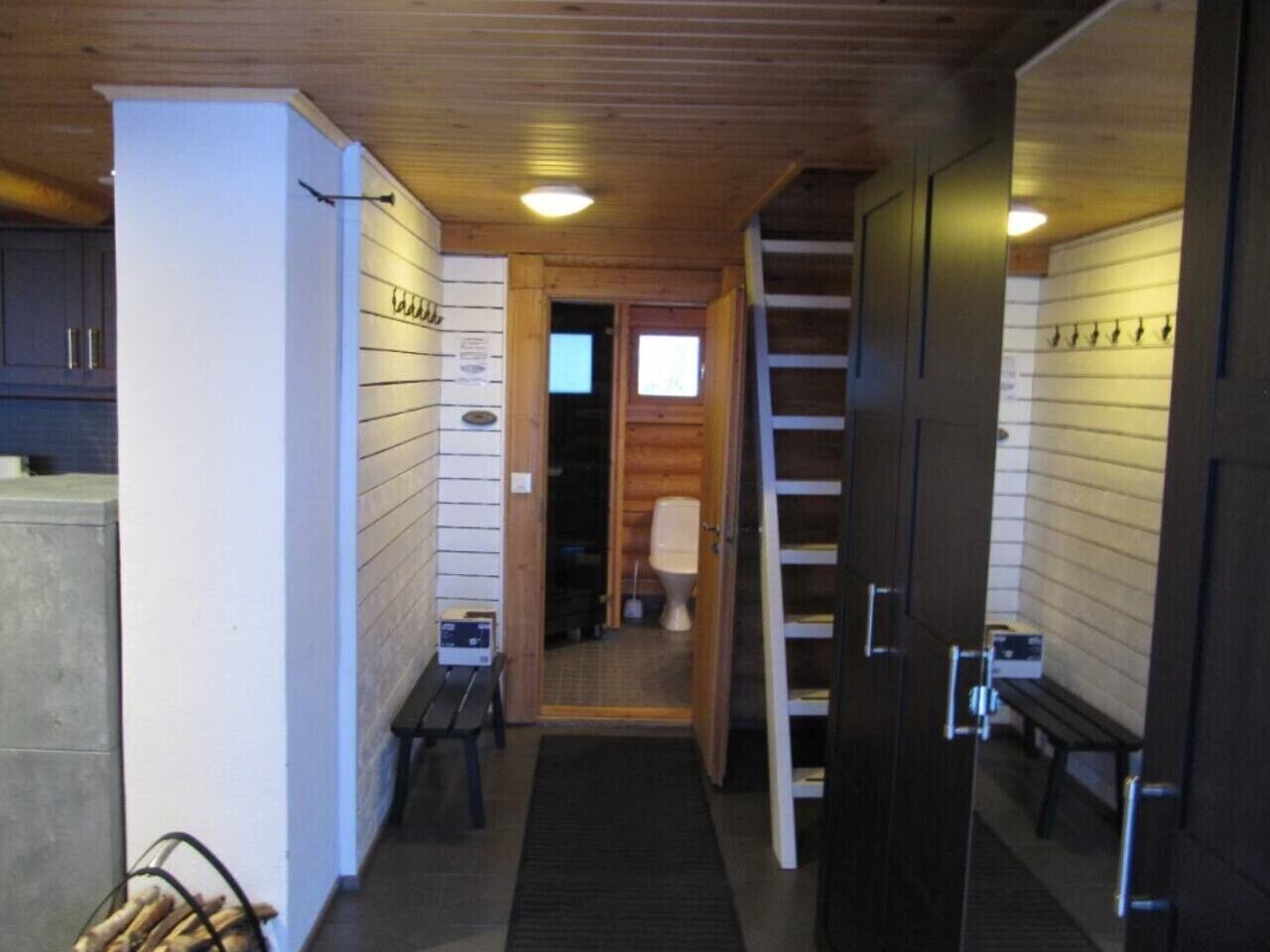 A narrow hallway with wooden walls, a bench, and a door leading to a bathroom.