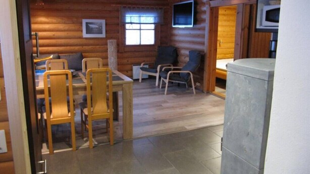 Ein Holzblockhaus-Innenraum mit Essbereich, einem kleinen Tisch und einem Fernseher.