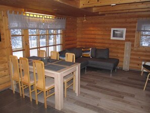 A log cabin interior with a dining table, chairs, a sofa, and a fireplace.
