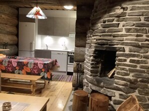 A rustic interior with a stone fireplace, wooden furniture, and a kitchen area. - Rantaruka | Atmospheric Apt | Sauna & Ski-Bus 100m (Ruka)