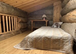 A cozy log cabin bedroom with a bed, a small table with a lamp, and a wooden railing. - Rantaruka | Atmospheric Apt | Sauna & Ski-Bus 100m (Ruka)