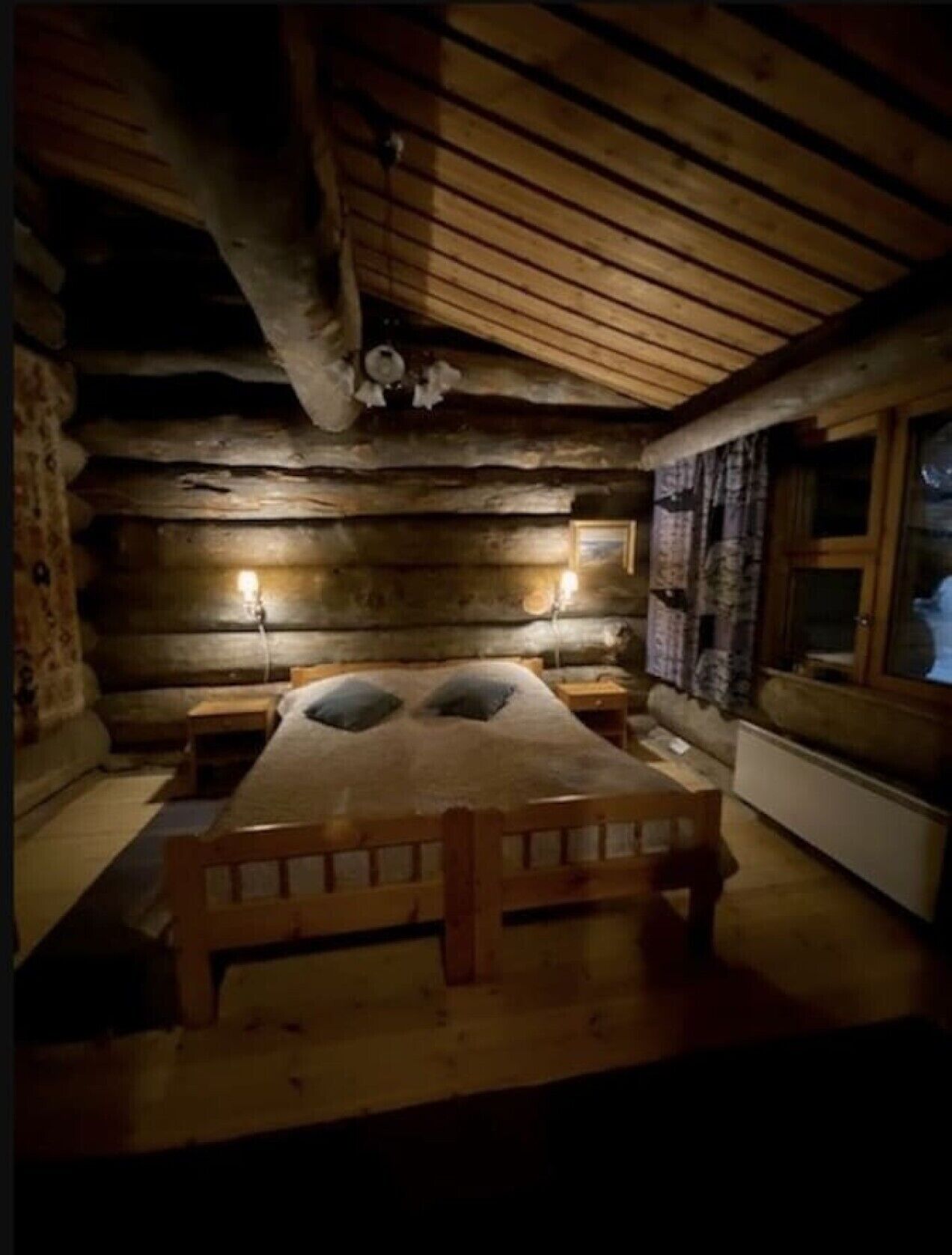 Double bed in the log-walled bedroom with a window and wall lamps.