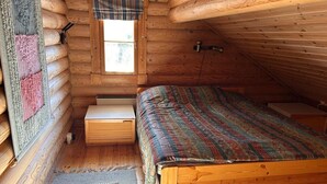 A log cabin bedroom with a wooden bed, a window with a plaid curtain, and a small wooden nightstand. - Cozy Lakeside Cabin for 12 | Sauna & Lappish Hut (Kuusamo)