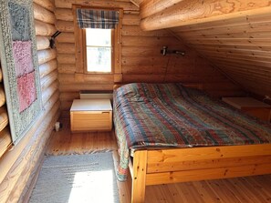 A log cabin bedroom with a wooden bed, a window with a plaid curtain, and a small wooden nightstand. - Cozy Lakeside Cabin for 12 | Sauna & Lappish Hut (Kuusamo)