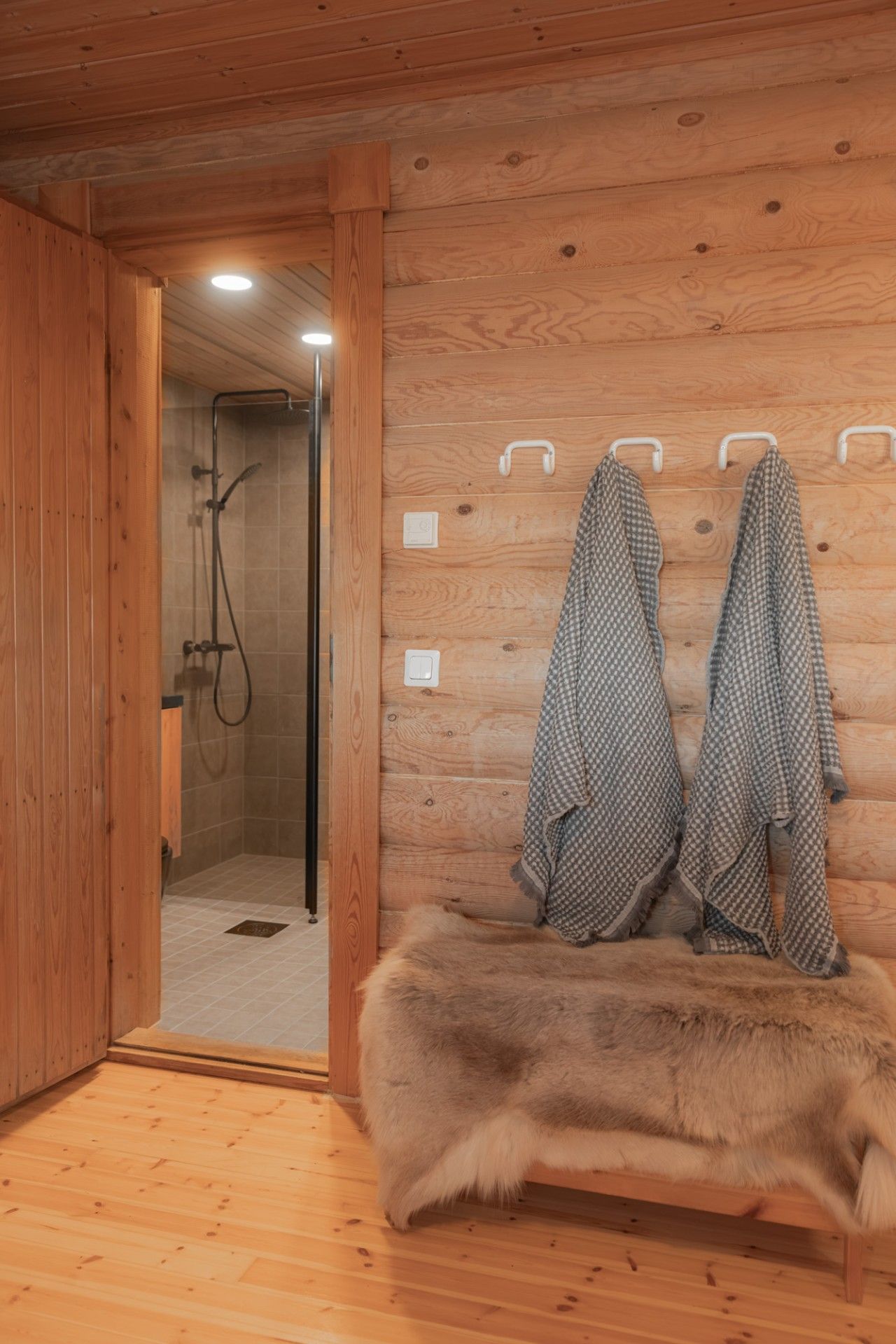 Ein Interieur einer Holzhütte mit einer mit Fell bezogenen Bank, einem Duschbereich und Handtüchern an Haken.