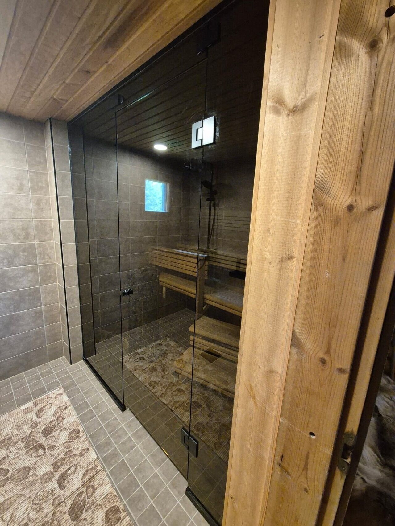 Un espace douche entièrement vitré, avec un banc à l’intérieur, des murs carrelés et un plafond en bois.