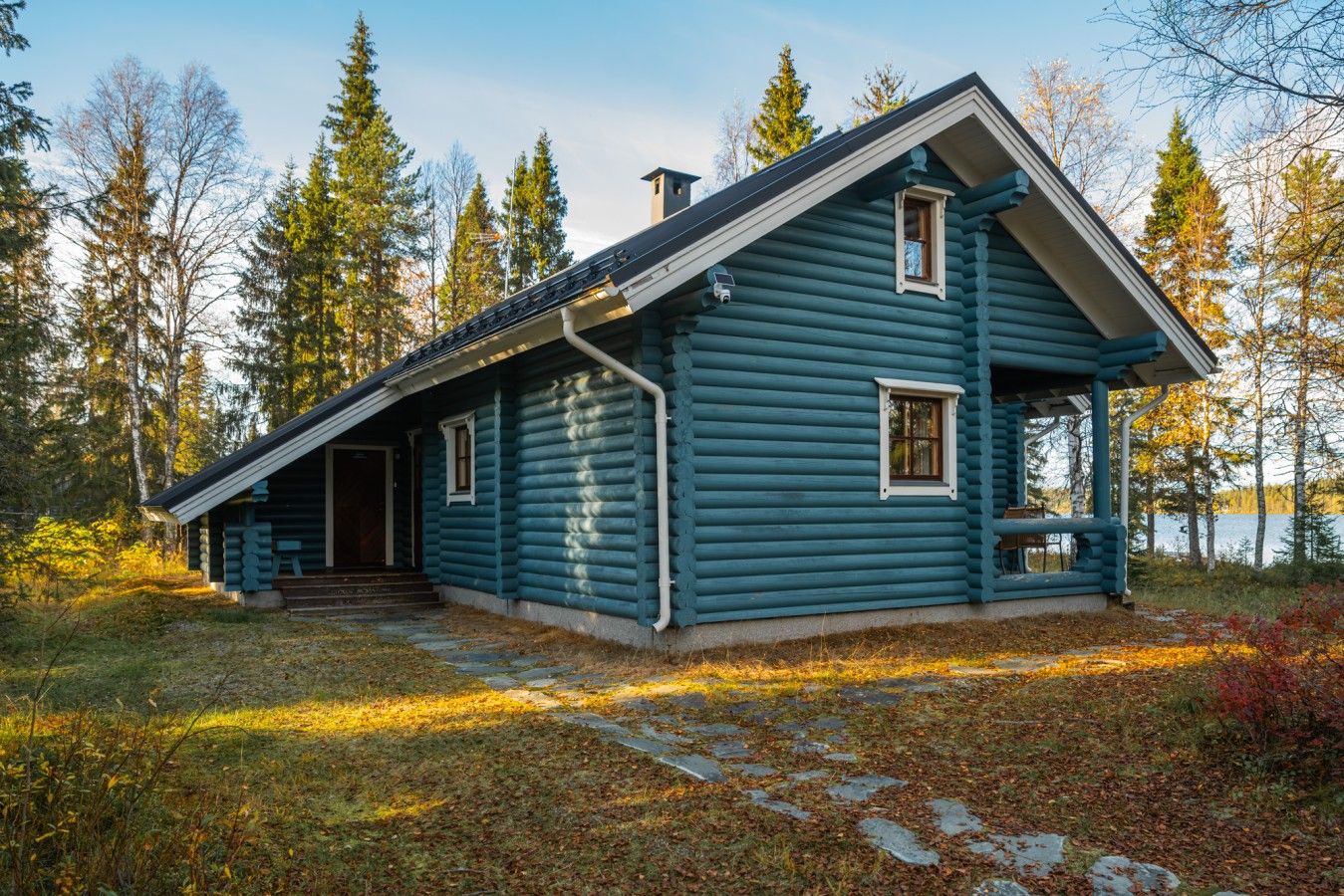 A log cabin with a porch, a chimney, and a view of a lake surrounded by trees.