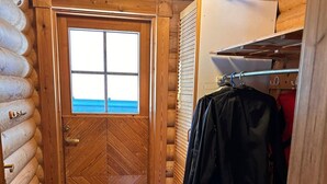 A log cabin interior with a wooden door, a window, and a clothes rack with jackets. - Cozy Lakeside Cabin for 12 | Sauna & Lappish Hut (Kuusamo)