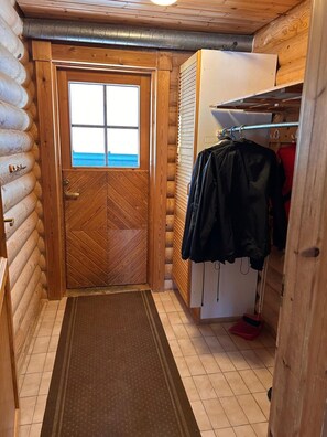 A log cabin interior with a wooden door, a window, and a clothes rack with jackets. - Cozy Lakeside Cabin for 12 | Sauna & Lappish Hut (Kuusamo)