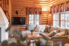 A cozy log cabin interior with a sofa, a fireplace, and a television.