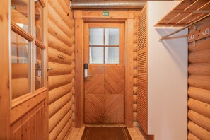 A wooden log cabin interior with a door, a window, and a white refrigerator.