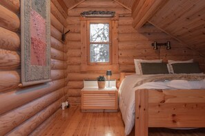A log cabin bedroom with a bed, bedside table, lamp, and a window.
