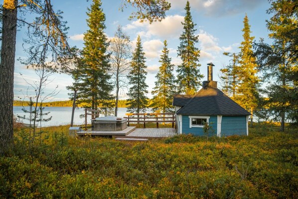 A cabin with a chimney, surrounded by trees and a lake.
