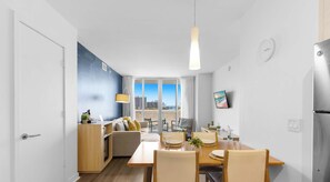 A modern kitchen with a built-in oven, a dining area with a wooden table and chairs, and a large window with a city view. - Cozy Spacious 1BR - Intracoastal View & Bay View (Hallandale Beach)