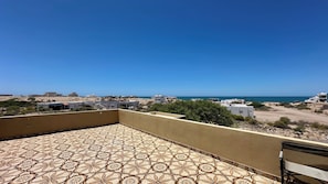 A rooftop terrace with patterned flooring, a view of the sea, and surrounding buildings.