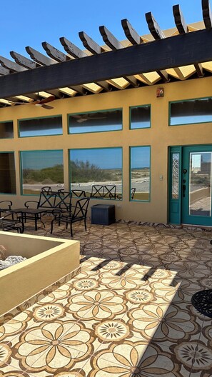 Un patio exterior con una pérgola, varios ventanales y piso de baldosas.