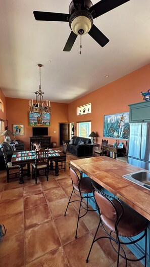 A spacious living area with a large dining table, a kitchen with a refrigerator, and a ceiling fan.