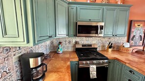 A kitchen with teal cabinets, a stainless steel microwave, a stove, and a coffee maker.