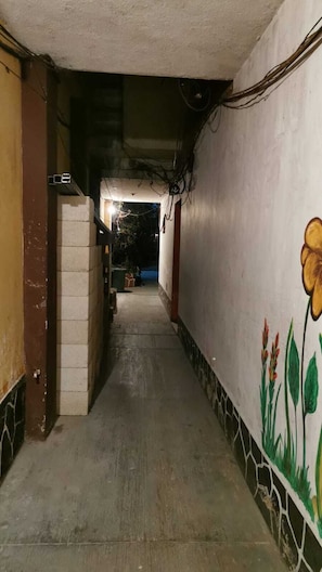 A narrow corridor with a tiled floor, walls with floral patterns, and a door at the end.
