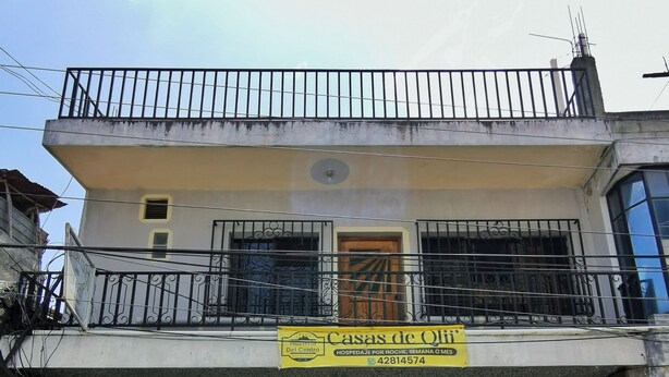 Un bâtiment à deux étages doté d’un balcon, d’une enseigne publicitaire indiquant « Casas de Oli » avec un numéro de téléphone, et d’un panneau « Stationnement interdit ».