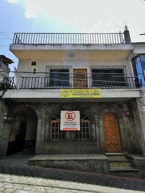 A two-story building with a balcony, a sign advertising 'Casas de Oli' with a contact number, and a 'No Parking' sign.
