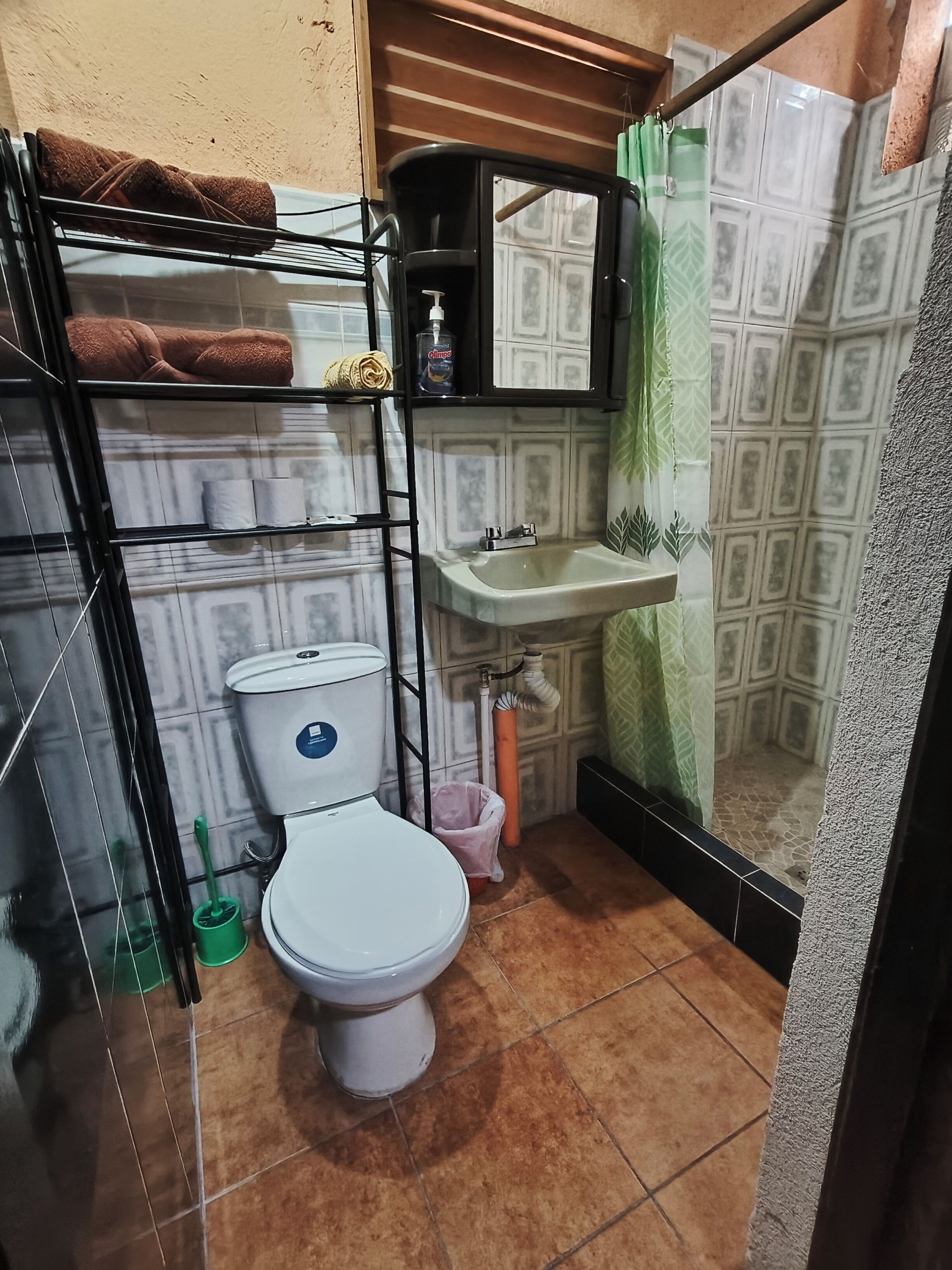 A compact bathroom with a toilet, a shelf with towels, a sink, and a shower area.