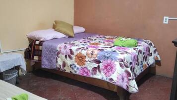 Uma cama de solteiro com colcha florida, um travesseiro e uma toalha verde no chão.