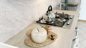 A kitchen with a gas stove, a kettle, and a decorative bowl on a woven mat. - Casa Lara by Ca-Sa Check (Aprica)