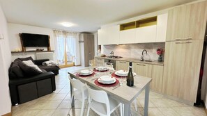 A modern kitchen with white cabinets, a dining table set for four, and a living area with a sofa and TV. - Casa Lara by Ca-Sa Check (Aprica)
