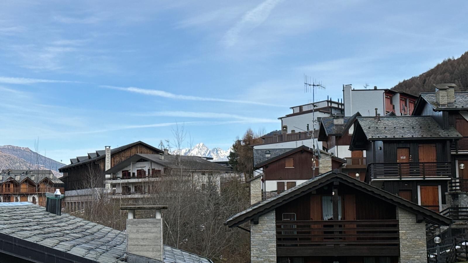 Un conjunto de edificios de madera de varios pisos, algunos con balcones, frente a un telón de fondo de montañas y un cielo despejado.