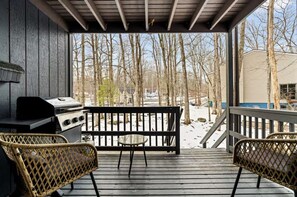 A covered outdoor area with a grill, two wicker chairs, and a view of a snowy landscape. - 4BR-Cozy Cabin | Hot Tub, Fire Pit & Game Room (East Stroudsburg)