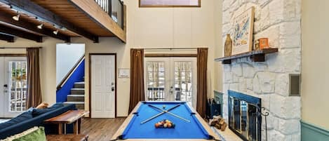 A pool table in a room with a stone wall, a fireplace, and a staircase.