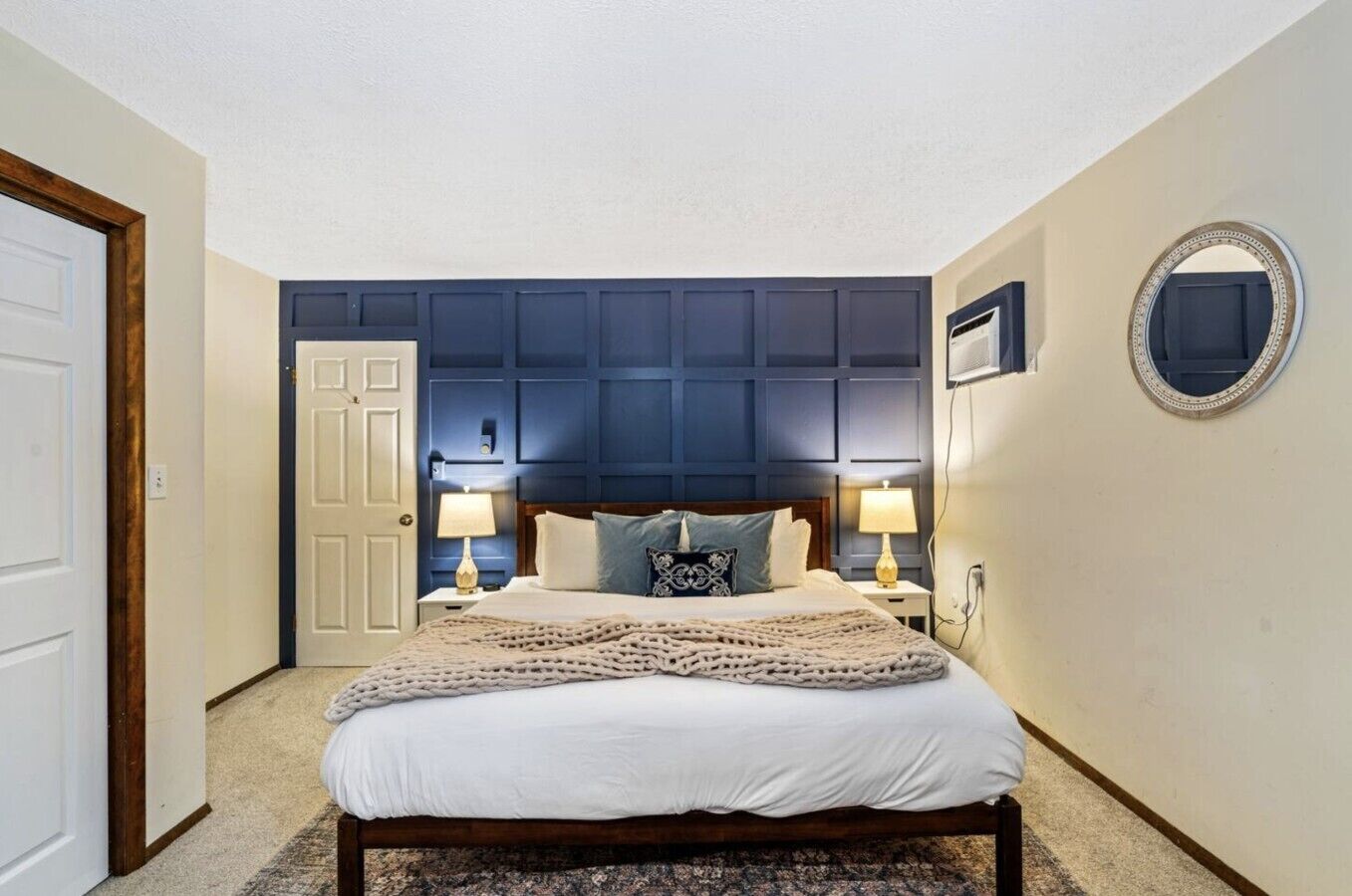 A bedroom with a bed, two bedside tables, a headboard, a mirror, and a door.