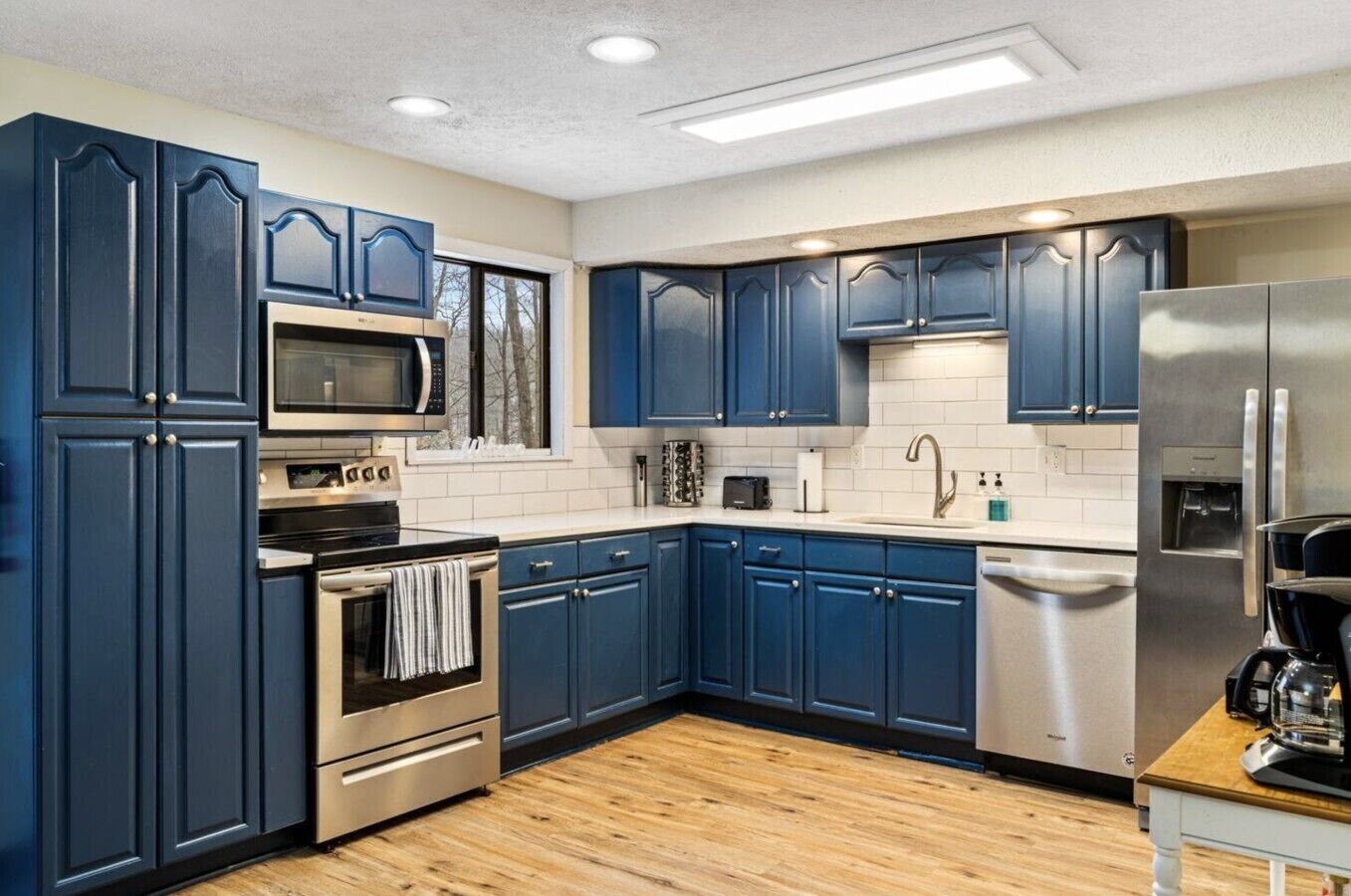 A modern kitchen with dark blue cabinets, stainless steel appliances, and a wooden floor.