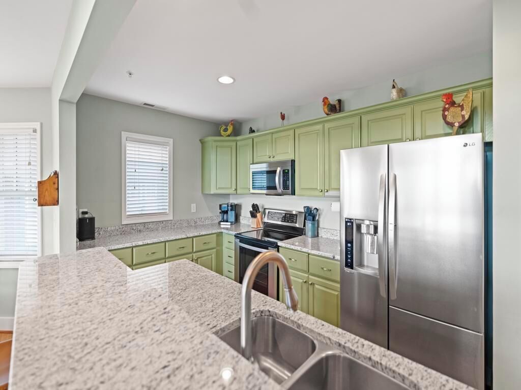A kitchen with green cabinets, stainless steel appliances, and a granite countertop.