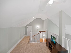 Um quarto no sótão com teto inclinado, escada de madeira, corrimão branco e um quadro em cima de um console de madeira.