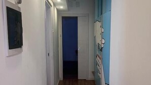 A narrow hallway with wooden flooring, white walls, and a blue door at the end.