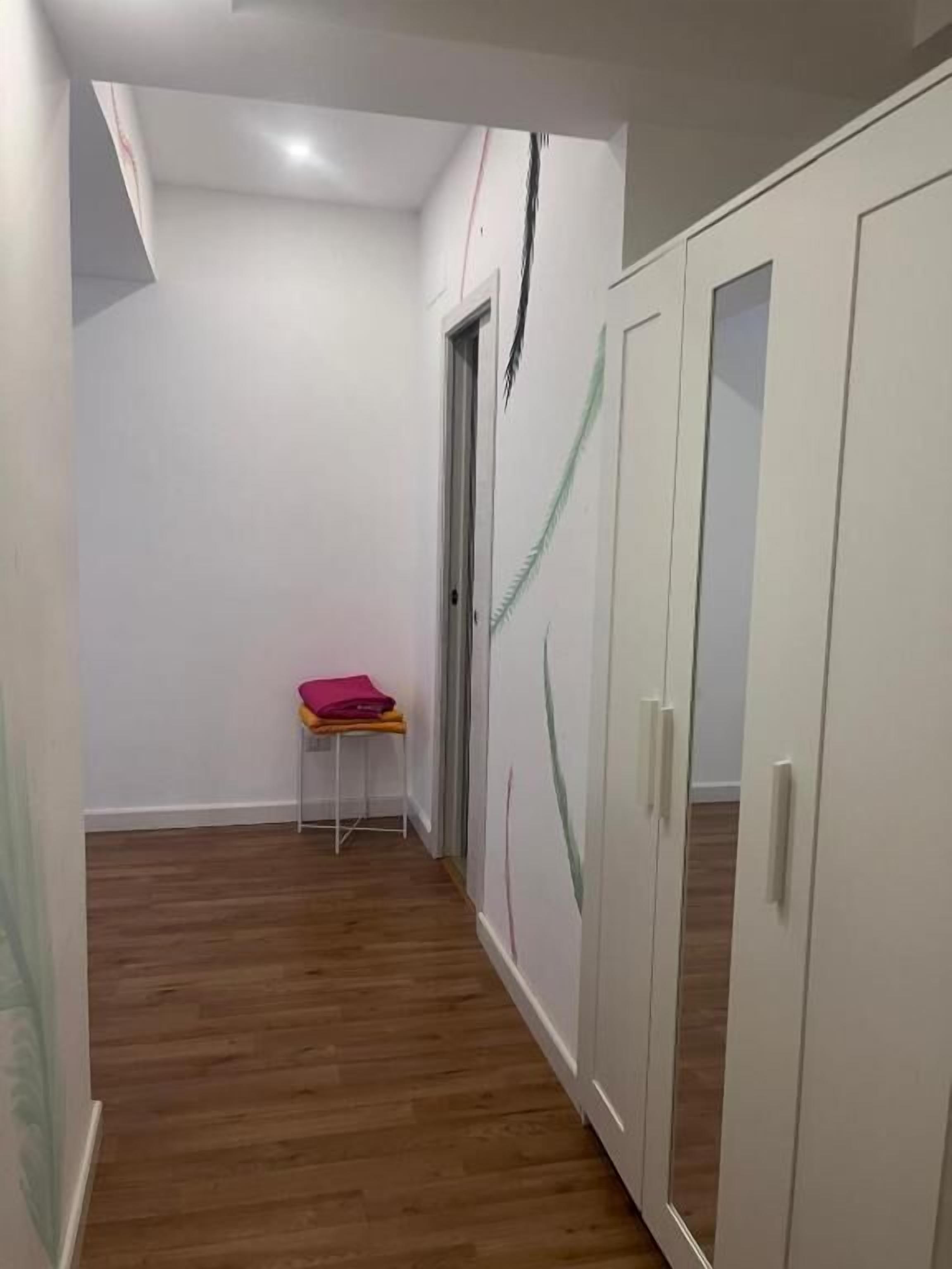 A narrow hallway with wooden flooring, white walls, and a door with a green curtain.