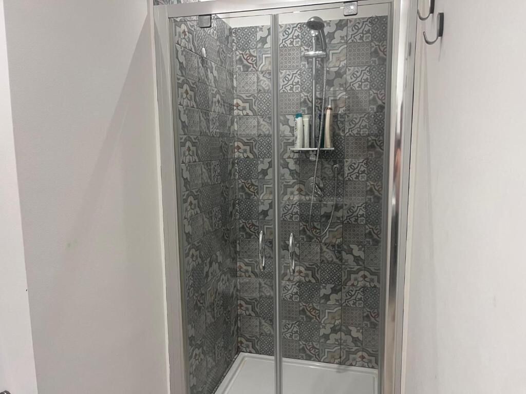 Een douchecabine met patroon betegelde wanden en een handdouche.