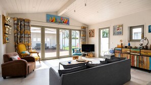 A spacious living room with a large sofa, a television, and a wooden cabinet with colorful artwork. - ODELINE maison spacieuse et lumineuse au calme (Le Bois-Plage-en-Ré)