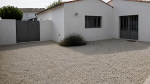 A modern building with a white exterior, a gravel driveway, a small bush, and a metal gate. - ODELINE maison spacieuse et lumineuse au calme (Le Bois-Plage-en-Ré)