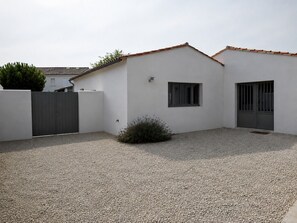 A modern building with a white exterior, a gravel driveway, a small bush, and a metal gate. - ODELINE maison spacieuse et lumineuse au calme (Le Bois-Plage-en-Ré)