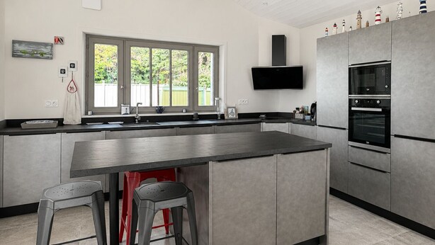 A modern kitchen with a large island, stainless steel appliances, and a window overlooking greenery. - ODELINE maison spacieuse et lumineuse au calme (Le Bois-Plage-en-Ré)